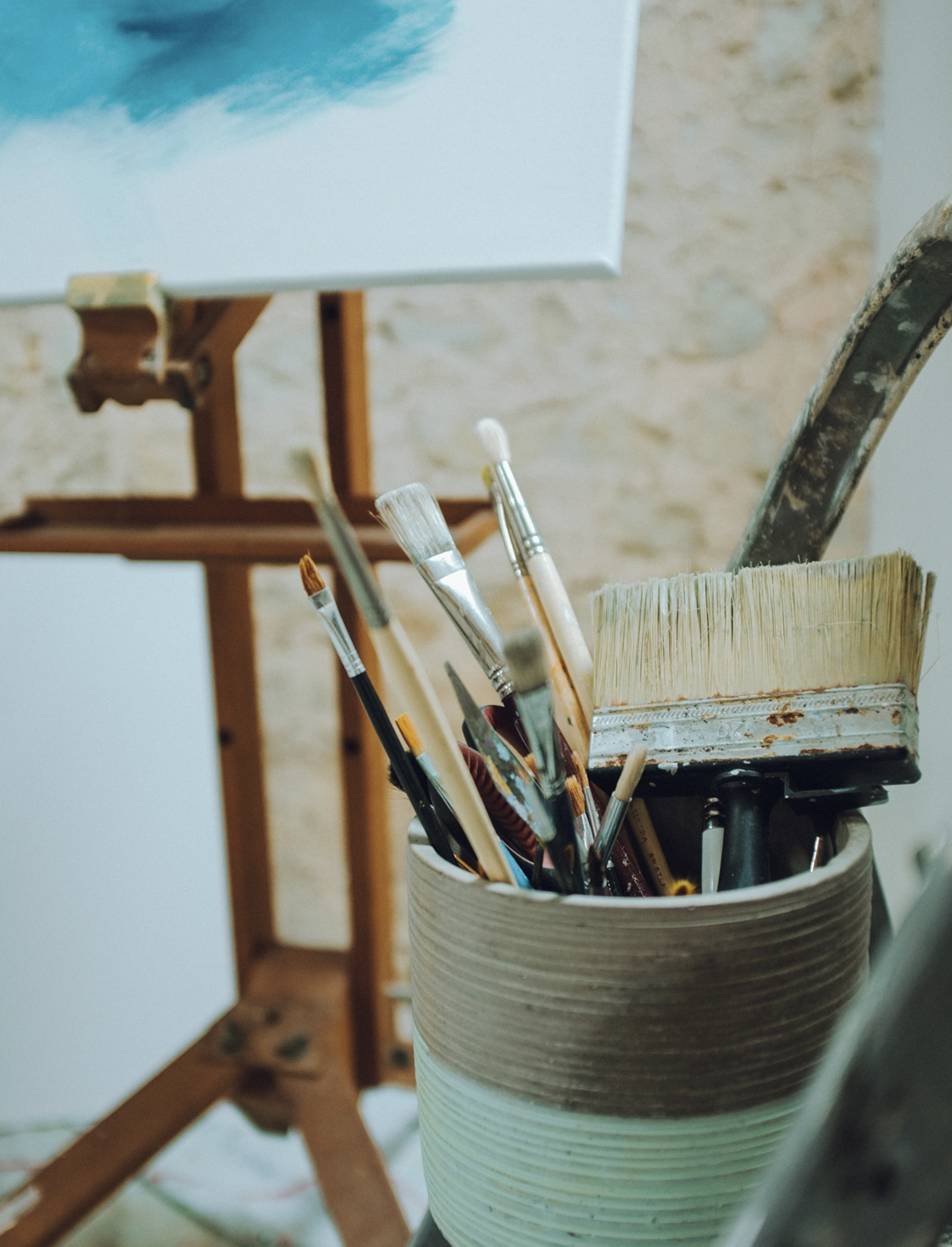 artist studio with pot of paint brushes and canvas in background